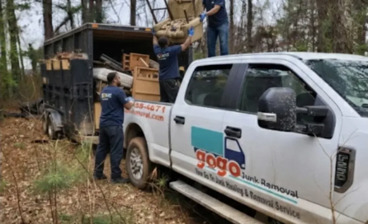 Three GoGo Junk Removal workers loading armchair into black trailer attached to white branded pickup truck