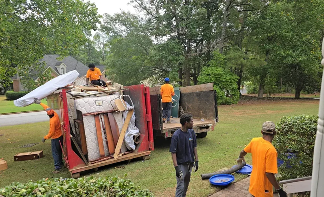 GoGo Junk Removal team loading mattresses and debris into red dumpster at residential property