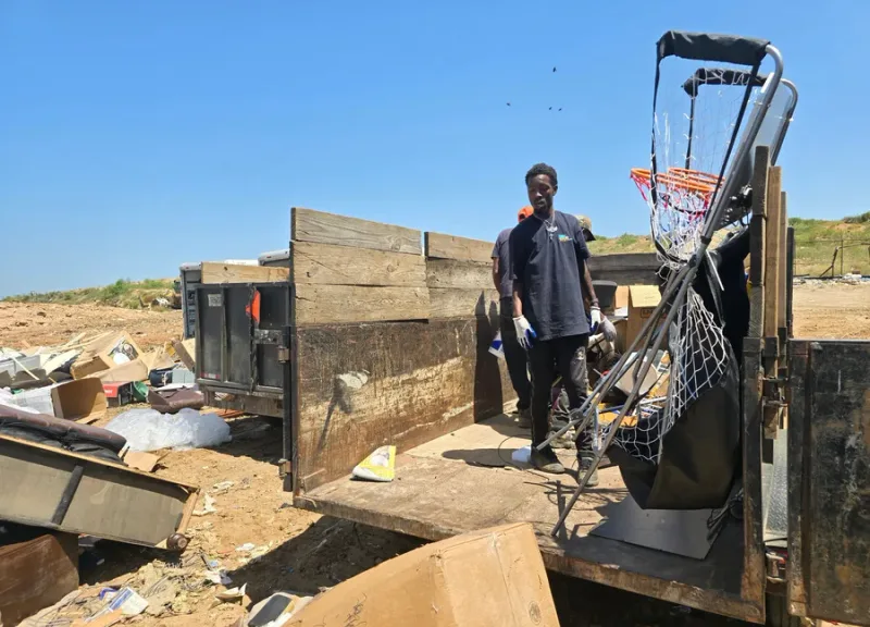 GoGo Junk Removal worker standing on loaded trailer with basketball hoop and discarded items