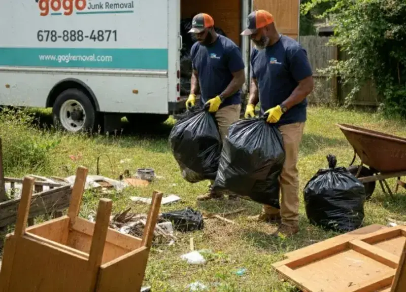 Two GoGo Junk Removal workers in branded uniforms lifting garbage bags during yard cleanout